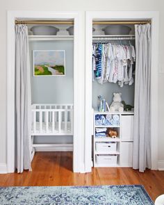 an open closet with clothes hanging on the doors and baby's crib next to it