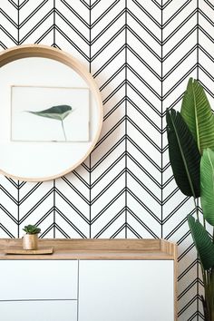 a white dresser with a mirror on it next to a green plant and wallpaper