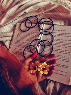 a person laying on top of a bed next to an open book with flowers in their hands