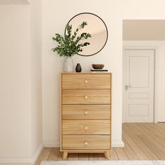 a white room with a wooden dresser and mirror on the wall above it is a potted plant