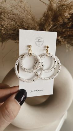 a pair of white earrings sitting on top of a table next to a vase with dry grass