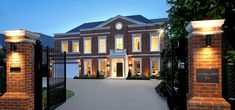 a large brick house is lit up at night with lights on the front gate and driveway