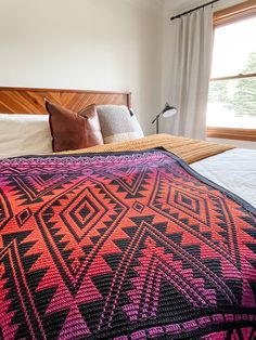 a bed with a colorful blanket on top of it next to a wooden headboard