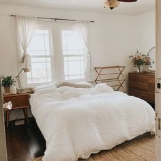 a bed sitting in a bedroom next to a window covered in white blankets and pillows