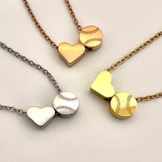 three heart shaped baseball pendants are shown on a white surface, one is gold and the other is silver