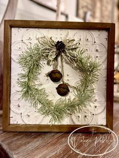 a close up of a christmas card with pine cones and greenery on it, hanging from a wooden frame