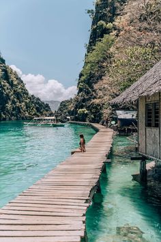 a person sitting on a dock in the water next to some mountains and houses with thatched roofs