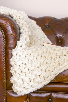 a white knitted blanket sitting on top of a brown leather couch