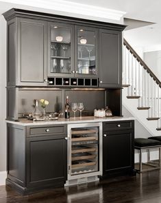 a kitchen with black cabinets and wine glasses on the counter, along with stairs leading up to the second floor