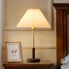 a lamp on a night stand next to a bed with a framed photo and an antelope