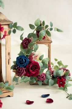 some red and blue flowers are next to a small lantern with green leaves on it