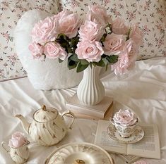 pink roses are in a white vase and tea set on a bed with floral sheets