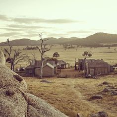 an old western town sits in the middle of a dry grass field with mountains in the background