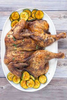 a whole chicken on a white plate with squash and zucchini garnishes