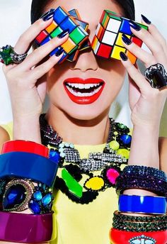 a woman holding up several pieces of colorful jewelry to her face and covering her eyes with both hands