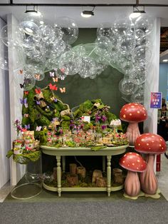 a table with mushrooms and plants on it in front of a display wall filled with balloons