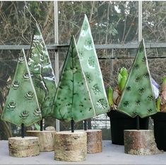 three green trees sitting on top of wooden logs in front of a glass wall and window