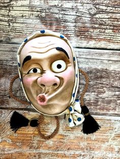 a mask with eyes, nose and mouth hanging from a rope on a wooden surface