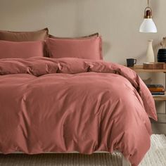 a bed with red sheets and pillows in a room next to a lamp on a table