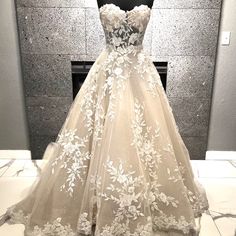 a wedding dress on display in front of a wall with white flowers and leaves all over it