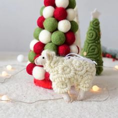 there is a small sheep standing next to a christmas tree with balls on it's back