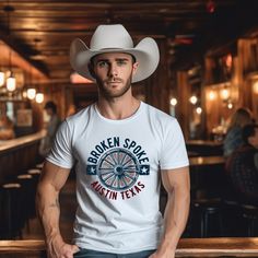 Pay homage to the legendary Broken Spoke in Austin, Texas, with our exclusive country music t-shirt. Featuring the iconic logo, this shirt embodies the honky-tonk's rich history and timeless charm. Wear it to carry the spirit of the Spoke with you wherever you go. Get yours now and dance to the rhythm of Austin! The Country Music Design studio collection features sharp & and funny designs inspired by the good times and country music,  the moments we take to rest and reboot, our adventures, and j Summer Graphic Print T-shirt For Country Events, Western Style Cotton T-shirt For Rodeo, White Western T-shirt For Rodeo, Western Style T-shirt For Ranch In Summer, Fitted Graphic Print T-shirt For Rodeo, Western Style Summer T-shirt, White Graphic Tee For Western-themed Events, White Graphic Print T-shirt For Western-themed Events, Fitted Graphic Print T-shirt For Ranch