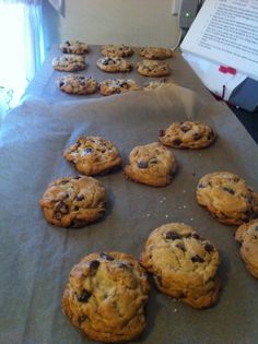 chocolate chip cookies are lined up on a sheet of parchment paper next to an open book