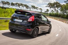 the rear end of a black car driving on a road with trees in the background