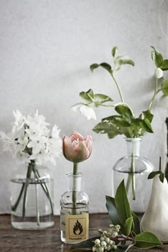 three vases with flowers in them sitting on a table next to other glass containers