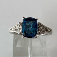 a fancy ring with a blue stone surrounded by white diamonds on a clear display case