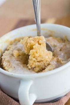 a white bowl filled with oatmeal on top of a wooden table next to a spoon