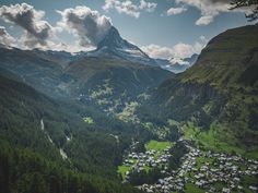 an aerial view of a mountain village in the valley with trees and mountains around it