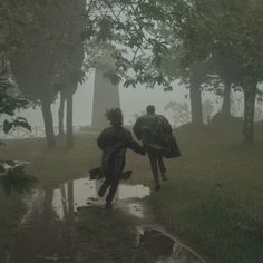 two people are walking in the rain near trees