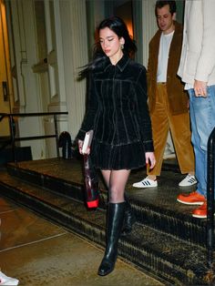 a woman in black dress and boots walking down stairs