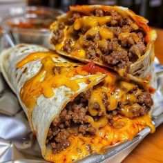 two burritos with meat, cheese and sauce on a tin foil wrapper