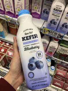 a person holding up a bottle of kefir blueberry milk in a store