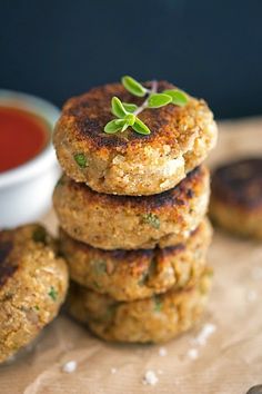 four crab cakes stacked on top of each other next to a small bowl of sauce