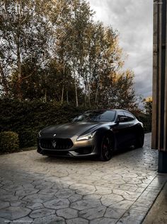 a black masera is parked in front of some bushes and trees on a cloudy day