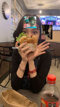 a woman sitting at a table with a sandwich in front of her face