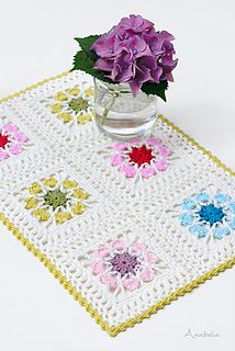 a crocheted table mat with flowers in a vase on it and a white background