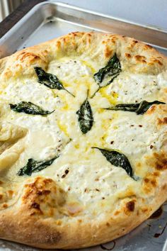 a pizza with cheese and spinach leaves on it sitting on a metal baking pan