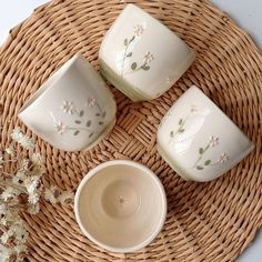 four white dishes sitting on top of a wicker basket next to a vase with flowers