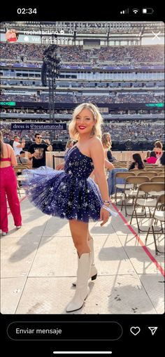 a woman in a blue dress and cowboy boots posing for a photo at a baseball game