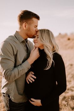 a pregnant couple cuddles and kisses while standing in the desert with their noses to each other