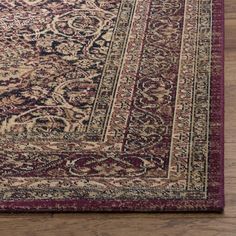 a red and beige area rug with an ornate design on the bottom, in front of a wooden floor