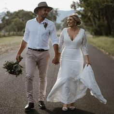 a man and woman are walking down the road holding hands while dressed in white dresses