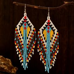 two pairs of beaded earrings hanging from a branch on a dark background with some rocks in the foreground