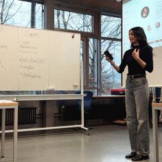 a woman standing in front of a whiteboard with writing on it and holding a cell phone