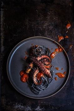 an octopus and pasta dish on a black plate with sauce drizzled over it