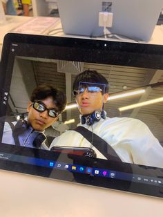 two men wearing headphones and glasses are on the screen of a laptop computer that is sitting on a desk